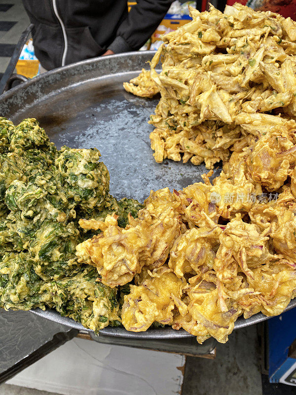 一堆酥脆的洋葱bhajis和palak pakora(菠菜馅饼)放在不锈钢的塔利(托盘)上，印度街头美食素食小吃，高架视野，重点放在前景